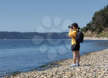 Woman photographer taking photos of the lake during bright summer day