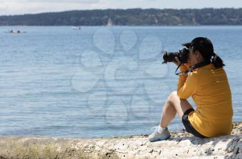 Woman photographer taking photos of lake with boats during bright summer day
