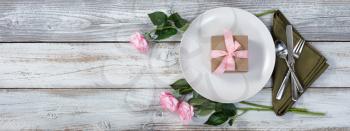 Romantic dinner setting with pink roses and gift box on rustic white wood in flat lay view