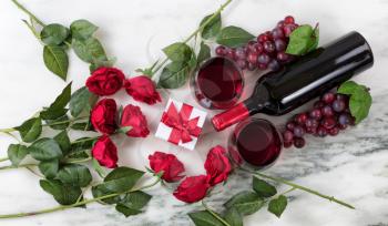 Overhead view of Red wine bottle, glasses, grapes and roses on natural marble stone setting