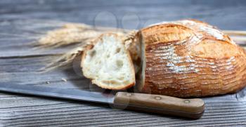 Close up view of a sliced baked whole loaf of bread with cutting knife and wheat stalks on rustic wooden boards