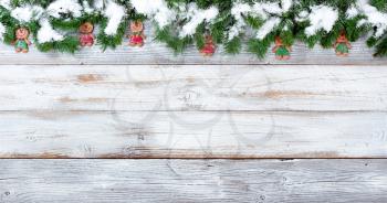 Snow covered top border of Christmas evergreen branches and cookie decorations on white vintage wood