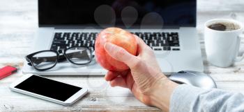 Close of male hand holding fresh apple with workstation technology in background for business or education use 