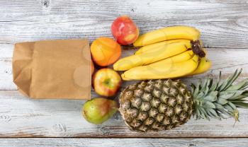 Fresh organic fruit spilling out of recyclable paper bag on white rustic wooden background 