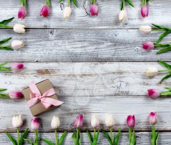 Happy Mothers Day holiday concept with brown gift box and border of pink tulips on white rustic wooden background  