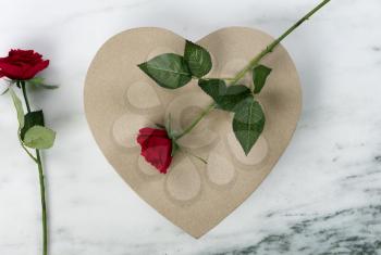 A large cardboard heart giftbox with red roses for Happy Valentines Day on a marble stone background    