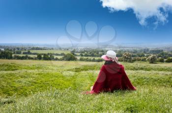Woman sitting down in grassy farm fields while looking at horizon 