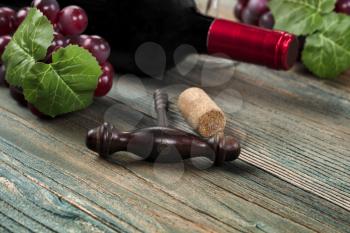 Select focus of vintage corkscrew with grapes and wine bottle in background on blue rustic wood planks