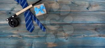 Fly fishing gear, neck tie and giftbox on faded blue wood for happy fathers day concept background 