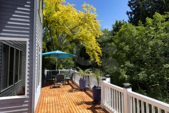 Home outdoor wood cedar deck with trees in full seasonal bloom and clear blue sky plus furniture and plants 