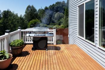 Large outdoor BBQ cooker with smoke coming out while on home wooden deck during summertime 