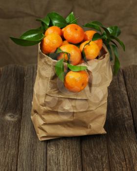 Fresh tangerines with leaves in recycle paper bag on wooden table. Closeup.