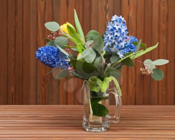 Bouquet from tulips and hyacinths in glass vase on wooden background.