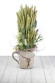 Still life of flowers and ears of rye in  vintage vase with keys isolated on wooden background.