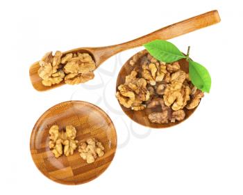 Handful of walnuts in wooden bowls, scoop and green leaves isolated on white background. Closeup. Selective focus.
