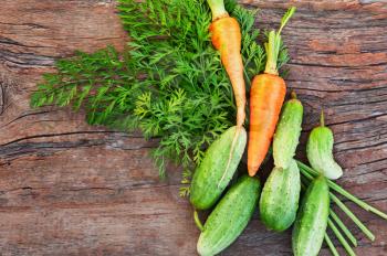 Juicy ripe green cucumbers and carrots on old wooden background. Closeup.
