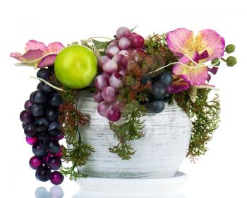 Colorful composition made of artificial flowers and fruits in an old glass vase isolated on white background.