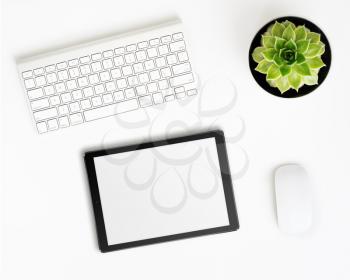 White office desk table with tablet pc computer with blank screen, wireless aluminum keyboard, mouse and succulent flower in pot. Top view with copy space. Flat lay.