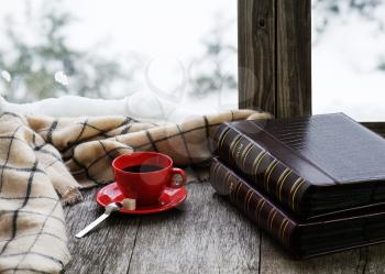 Red cup of coffee or tea with a metal spoon, piece of sugar and two photo albums located on a stylized wooden windowsill. Winter concept of comfort and relaxation.