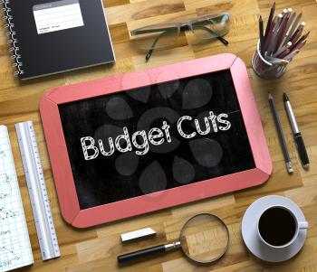 Budget Cuts Handwritten on Red Chalkboard. Top View Composition with Small Chalkboard on Working Table with Office Supplies Around. Budget Cuts Concept on Small Chalkboard. 3d Rendering.