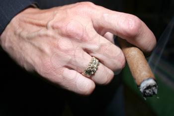 Hand holding a cigar with a gold ring on a finger
