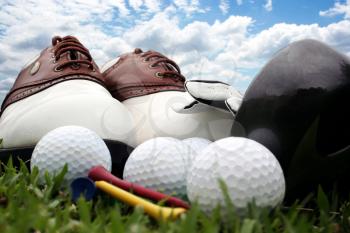 Golf shoes and equipment sitting on grass with a bright blue sky in the background