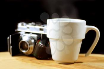 Macro shot of a steaming cup of coffee with an analog camera and roll of film in the background