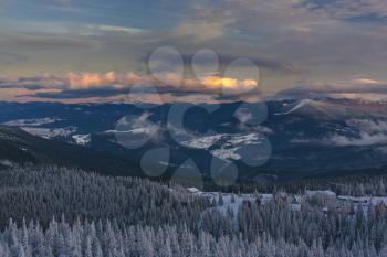 The trees covered by snow and the orange clouds over the mountains. The sun is coming down. Carpathian mountains, Ukraine.