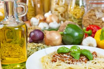 Spaghetti Bolognese with olive oil, Parmesan cheese, basil garnish various Italian pasta and ingredients out of focus in the background.