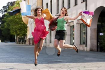 Two women being friends shopping downtown with colorful shopping bags, they are jumping for joy