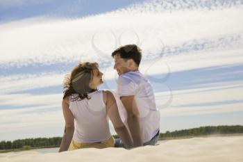 Rear view of relaxing couple sitting on sandy beach and smiling at each other