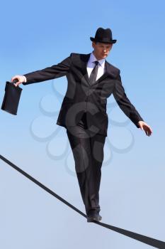 Photo of skilled businessman walking down ribbon or rope with blue sky at background 