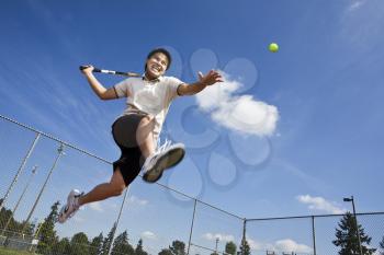 An asian tennis player jumping in the air hitting a tennis ball