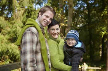 Portrait of happy family of three smiling at camera on sunny day in park.