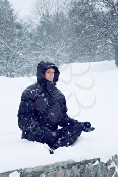 A young man meditates in the lotus position on the snow