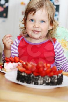 The little blue-eyed girl eating cake with strawberries