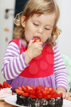 The little girl eating cake with strawberries