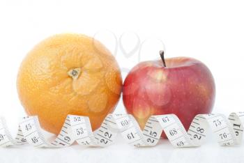 Orange and apple with a measuring tape on a white background.