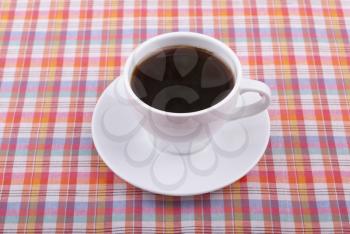 Cup of coffee on a checkered tablecloth.
