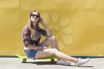 Stylish young girl sitting on a skateboard.