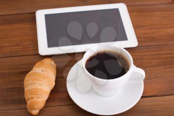 Cup of coffee and a croissant digital tablet on the table.