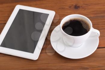 Digital tablet and cup of coffee on wooden desk.
