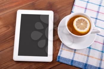 Tablet computer a cup of tea with a lemon on the table.