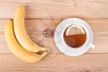 Bananas and a cup of tea on a wooden table. Top view .