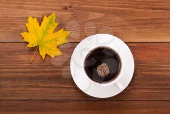 Cup of coffee and yellow maple leaf on a wooden background.