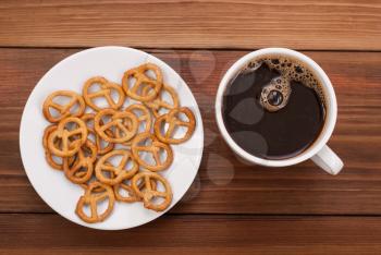 Cup of coffee and tasty pretzel on a wooden background.