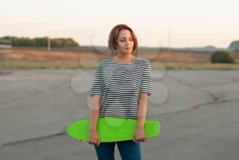 Beautiful young girl in a shirt with a skateboard in hands.