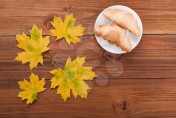 Croissants and maple leaves on wooden background.