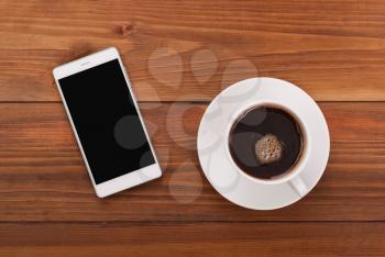 Cup of coffee and mobile phone on a wooden background. Top view.