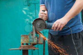 The worker cuts off a strip of metal, hand-held by an electric saw.